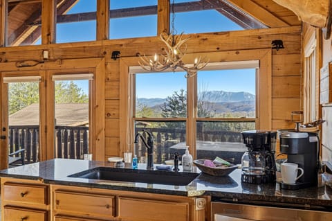 Imagine brewing your morning coffee while the Great Smoky Mountains fill your kitchen window | This Gatlinburg-area cabin kitchen features granite countertops, an antler chandelier, dual coffee makers & breathtaking panoramic Tennessee mountain views
