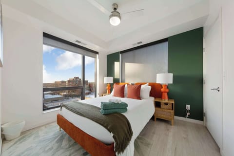 A cozy and modern bedroom featuring a comfortable bed with stylish linens and vibrant pillows. Large windows allow plenty of natural light, creating a bright and relaxing atmosphere for a restful night’s sleep.