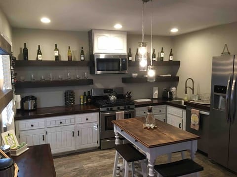 This gorgeous guest unit kitchen is packed with amenities, featuring a full gas range, stainless steel appliances, and charming open shelving for wine and glassware. The movable farmhouse table offers a delightful spot for prep and dining.