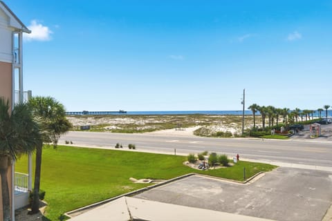 The property sits just across from coastal dunes and the Gulf, with palm-lined streets leading to white sand beaches visible beyond the main road.