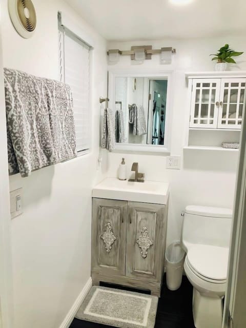 This compact, stylish bathroom features a unique rustic-finish vanity, a bright mirror with modern lighting, and a clever glass-front cabinet for extra storage, offering guests a clean and convenient private space.