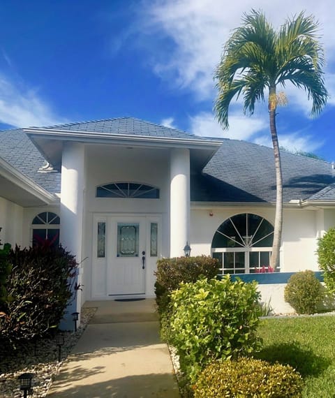 Front facade of the home featuring white columns, arched window, covered entry, and lush tropical landscaping