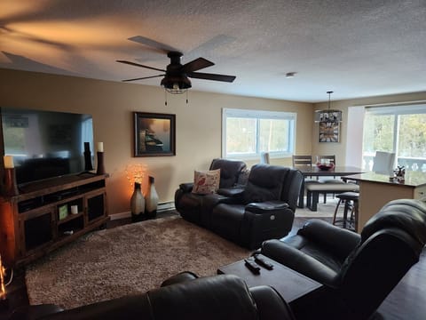 Living room space. 4 reclining leather chairs. TV, open to Kitchen and dining.