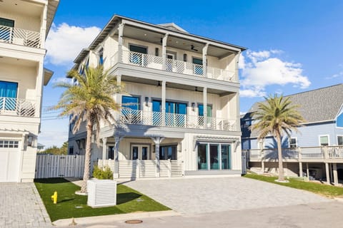 Modern three-story coastal home with palm trees and distinctive blue accents in a sunny beachside neighborhood.