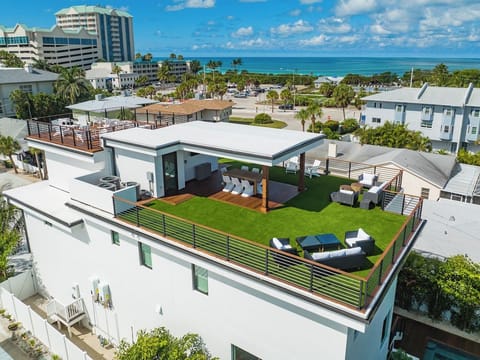 Aerial view of the modern coastal home showcasing expansive rooftop space, sleek architecture, and ocean glimpses nearby. This elevated perspective highlights the home’s prime location, outdoor living areas, and upscale island atmosphere.