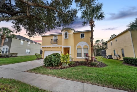 Explore a charming exterior with a warm yellow facade and elegant archways, surrounded by lush greenery and palm trees. The inviting entryway welcomes you, and the vibrant sunset adds a stunning glow to the atmosphere.