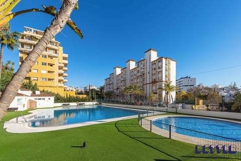 Residential complex with twin pools, palm trees, and sunny balconies. Bright design blends leisure and urban living.