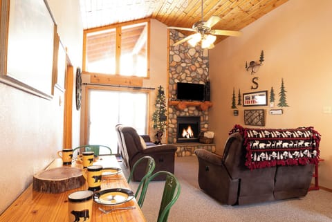 Relax in your warm living room with vaulted wood ceilings, a cozy stone fireplace, and natural light streaming through tall windows—perfect for mountain getaways.