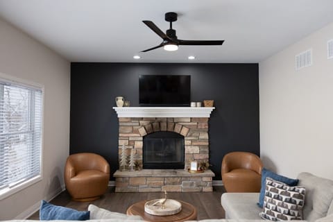 The inviting living room features a charming stone fireplace framed by modern decor and cozy seating, perfectly embodying the warmth and comfort of a beloved lake-town retreat.