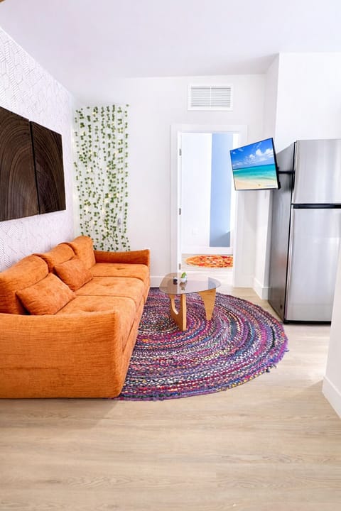 Unwind in the modern living room with orange Sofa, Smart TV, fridge, and rug.   