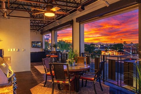 Rooftop deck boasts an outdoor kitchen with grill, sink, mini fridge, and cooking utensils, outdoor dining for four, a fireplace, smart TV, and three furnished lounging areas, and breathtaking panoramic views of Old Town Scottsdale.