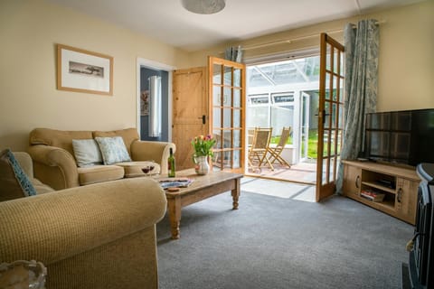 Lounge with sofas, coffee table and TV on unit, double door open into conservatory