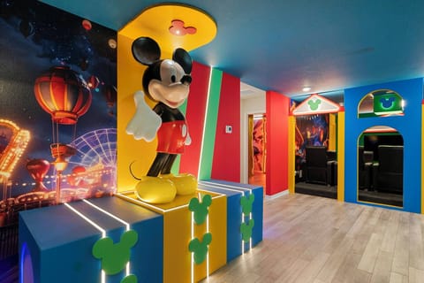 Welcome to a vibrant playroom filled with color, highlighted by a striking Mickey Mouse centerpiece and imaginative wall murals. The bold blue and yellow accents make this space perfect for energetic family fun.