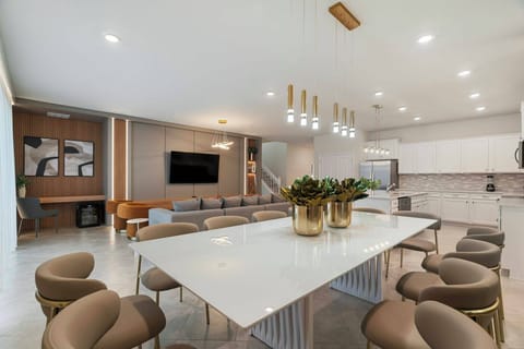 Experience our inviting dining area with a sleek white table and cozy rounded chairs perfect for gatherings. Elegant pendant lights add warmth to the modern decor, seamlessly connecting to the kitchen for a delightful atmosphere.