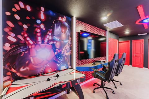 Welcome to a vibrant entertainment room with striking red accents and sleek black walls, ideal for game nights. Enjoy the lively wall mural and comfortable gaming chairs that invite hours of fun and relaxation.