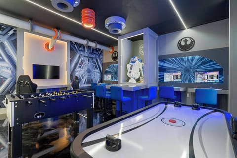Welcome to our vibrant game room, where a sleek foosball table and air hockey setup await you. The bold blue accents and stylish lighting create an energetic atmosphere, inviting fun and competition for guests of all ages.
