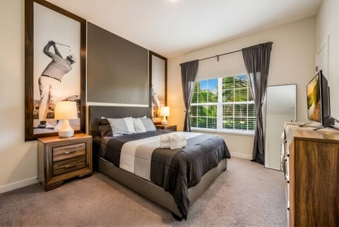 This cozy bedroom boasts a plush dark bed with fresh linens, stylish nightstands, and modern lamps that create a warm atmosphere. Large windows welcome natural light, enhancing the contemporary decor and offering a lovely view.