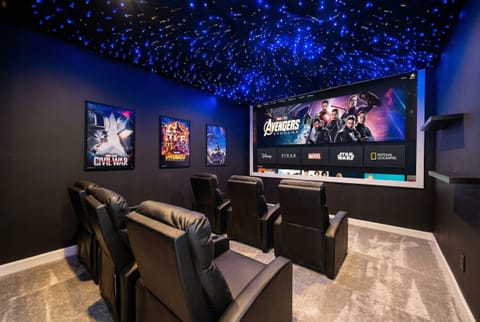 Enjoy a private movie theater with plush leather recliners, a large screen, superhero decor, and a glowing starry ceiling, creating a cozy space for family movie nights.