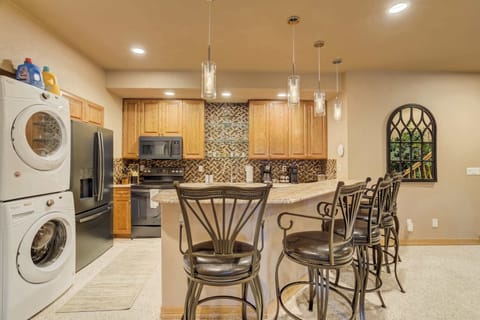 The fully equipped kitchen is designed for efficiency and convenience, featuring professional-grade appliances and a sleek breakfast bar with high-backed seating. The in-unit laundry station is neatly integrated for easy access.