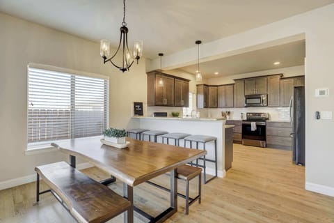 The open-concept dining area features a large natural wood table with bench seating, offering a perfect view of the modern kitchen and the breakfast bar.