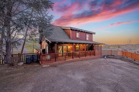 A charming log cabin retreat illuminated against a stunning pink and orange sunset sky, surrounded by peaceful mountain forest.