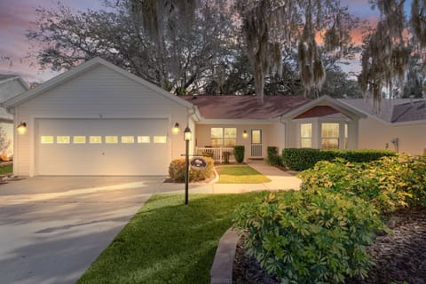 A charming single-story home nestled under majestic oak trees with Spanish moss, featuring well-maintained landscaping and warm evening lighting.