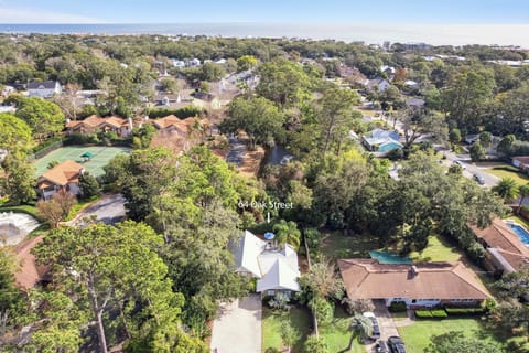 Aerial view of a charming neighborhood property on Oak Street, nestled among mature trees with the beach visible in the distance.