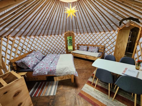 Spacious yurt interior w/ multiple beds & a dining nook under vaulted beams.