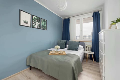 A cozy bedroom with a double bed, pastel-green wall, two framed pictures, and a small desk by the window.