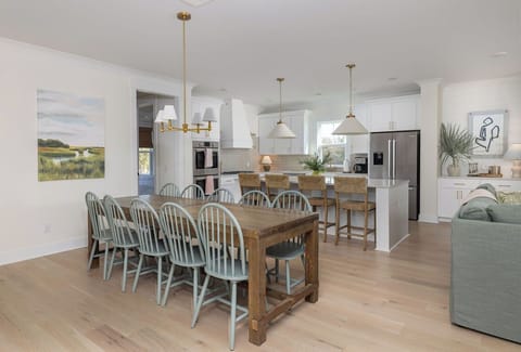 Your open-concept space seamlessly blends dining and kitchen with coastal charm, featuring a farmhouse table for eight and modern appliances.