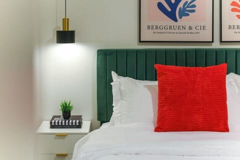 King bedroom with a plush green velvet headboard, crisp white linens, and a bold red accent pillow