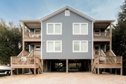 Modern coastal duplex with elevated design and natural wood accents, surrounded by mature trees in a peaceful neighborhood setting.