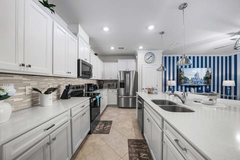 Chef-ready kitchen with crisp white cabinets, mosaic backsplash, stainless appliances, and a long quartz island with dual sinks-perfect for cooking and conversation.