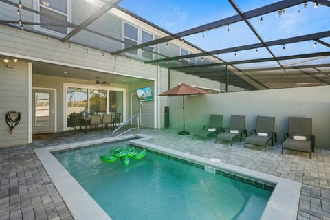 Unwind on the private screened lanai-sparkling pool, sun loungers with umbrella, and a covered dining area with ceiling fan and TV. String lights set the mood for al fresco evenings.