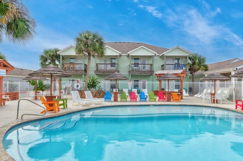 Tropical resort property featuring a curved swimming pool surrounded by colorful Adirondack chairs and palm trees under blue skies.