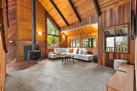 Cozy forest-view living room with a stone fireplace, game table, and vaulted ceilings.