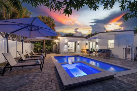 Heated pool and hot tub lit at dusk, with loungers on the paver deck.