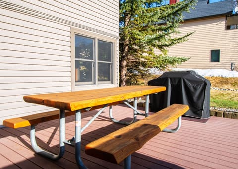 Wooden picnic table beside a grill on a small deck area outside the building.