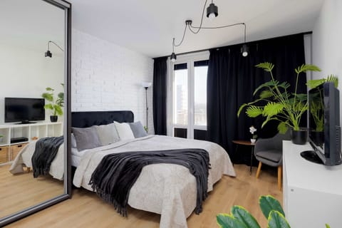 Bright studio interior with a double bed, soft textiles, and natural light from large windows.