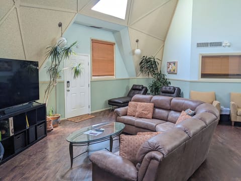 TV, couch, 2 brown sofa beds, 2 yellow chairs, door leading to back balcony