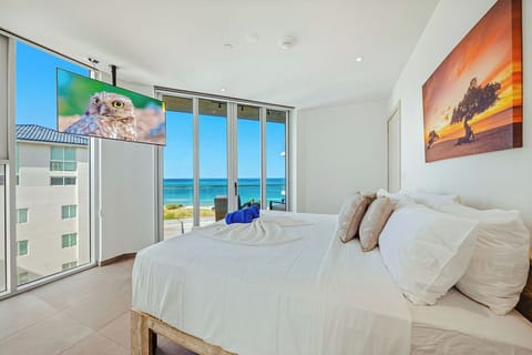 Wake up to breathtaking ocean views through floor-to-ceiling windows in your serene white bedroom, complete with cozy linens and stunning artwork.