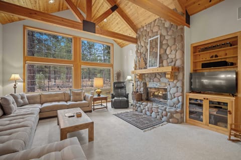 Unwind in your spacious living room with soaring vaulted ceilings, cozy stone fireplace, and forest views through large windows.