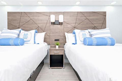 Bright, modern bedroom with two cozy queen beds, stylish wood accent wall, soft linens, bedside lighting, and blackout shade—perfect for a restful stay.