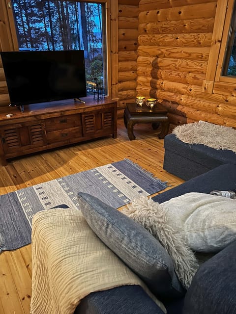 The bright, open-plan living area features authentic log walls and a large, comfortable sofa for relaxing afternoons.