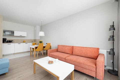 A minimalist lounge space with a coral sofa, light wood flooring, and clean white walls creating an open feel.