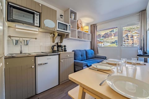 Sunny living room with sofa and dining table facing mountain views — ski-in/ski-out area Rue de Caron studio, sleeps 4.
