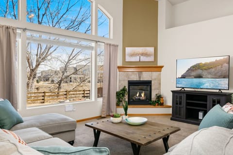 Unwind in your bright living room with cozy fireplace, large TV, and peaceful neighborhood views through expansive windows.