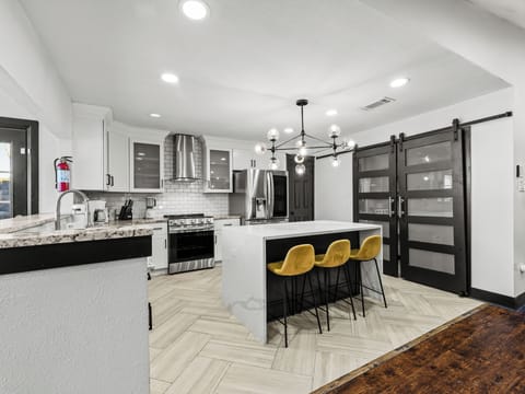 Your modern kitchen awaits with granite countertops, stainless steel appliances, and cheerful yellow bar stools perfect for morning coffee or evening meals.