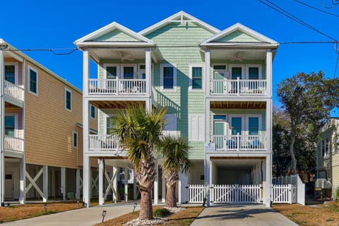 Charming mint green coastal property features multiple levels with covered parking underneath and white railings framing each floor.