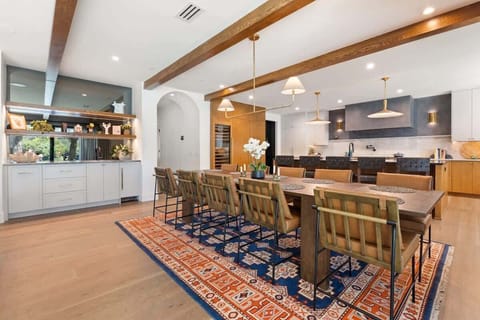 This dining space for 10 pairs modern elegance with warmth, featuring exposed wood beams, sleek lighting, and lake views. A bold rug anchors the table, while the wet bar with nugget ice machine makes entertaining effortless and refined.